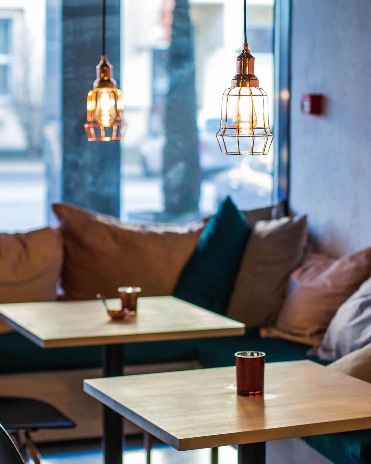 Salão de café com luminárias acesas e mesas de madeira à luz da manhã